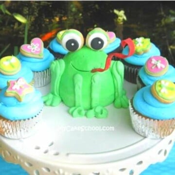 Little Frog Cake on pedestal, surrounded by cupcakes