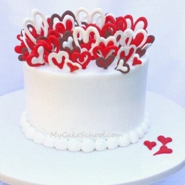 Cake on white pedestal, topped with lots of red and white chocolate hearts, placed vertically