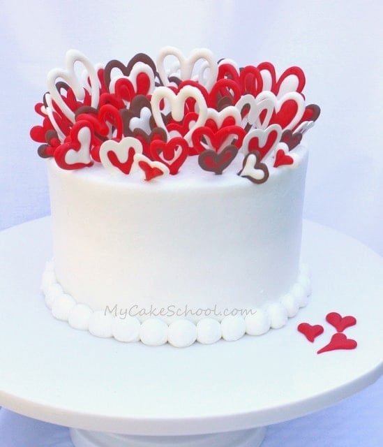 Cake on white pedestal, topped with lots of red and white chocolate hearts, placed vertically