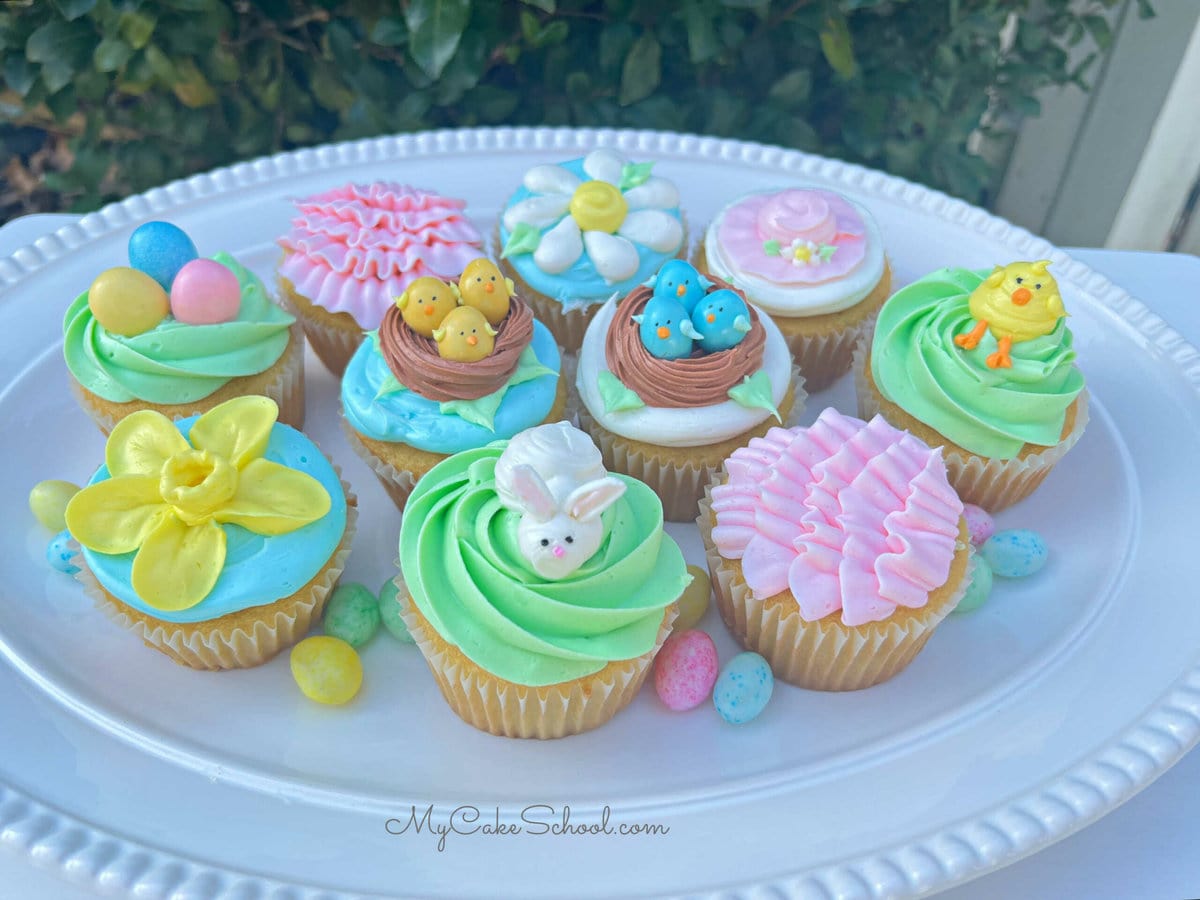 Assorted decorated Easter Cupcakes on a white platter.