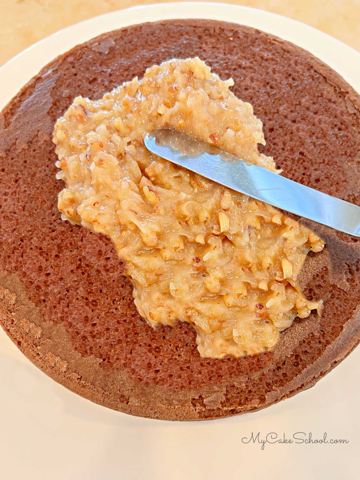 Spreading German Chocolate Cake with Coconut Pecan Filling using a small offset spatula.