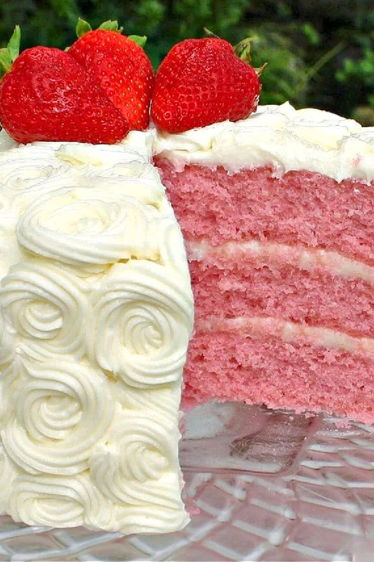 Closeup of a sliced strawberry cake, frosted with cream cheese frosting on a glass pedestal.