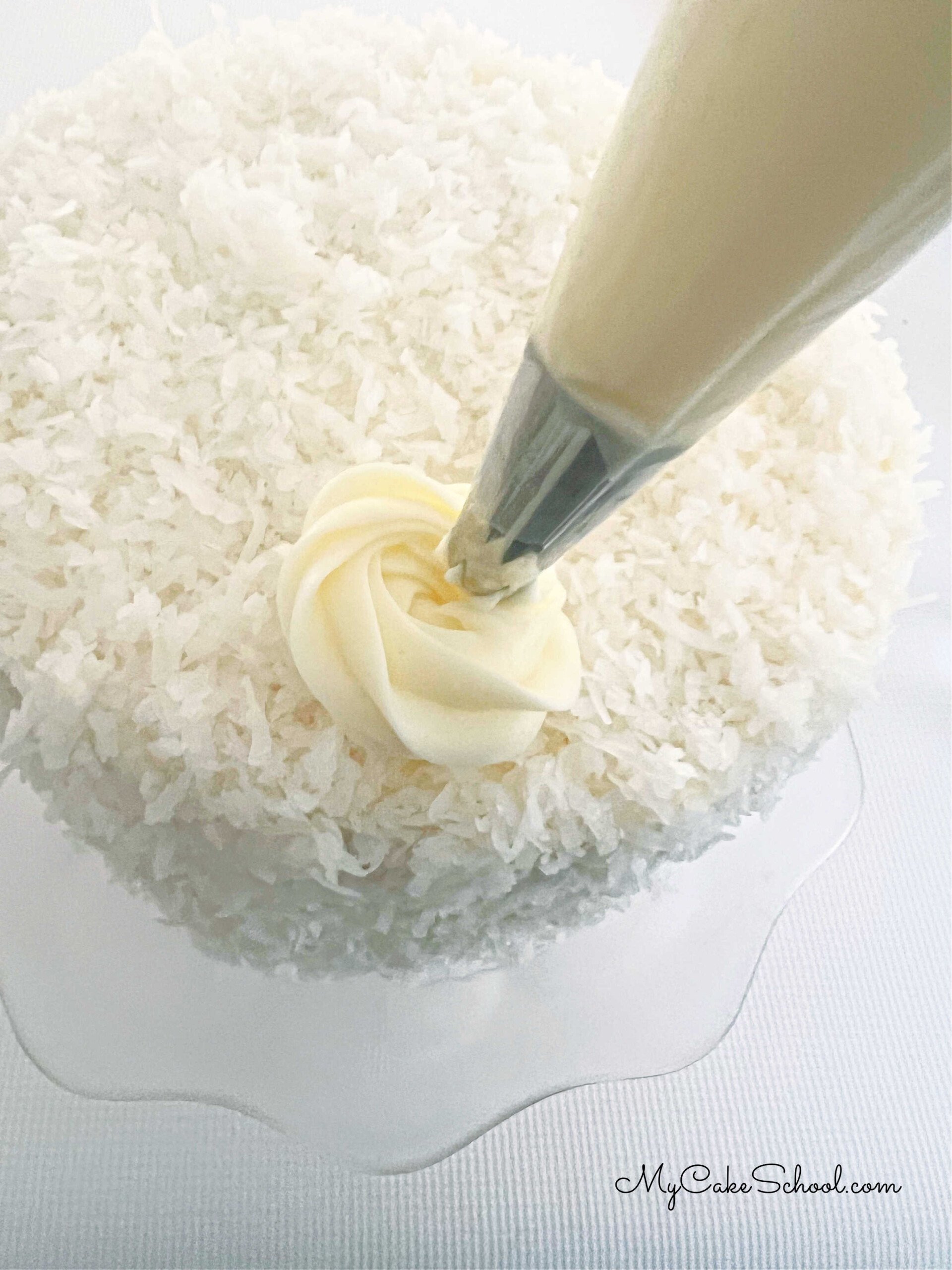 Piping a swirl of frosting onto the coconut-covered Pina Colada Cake.