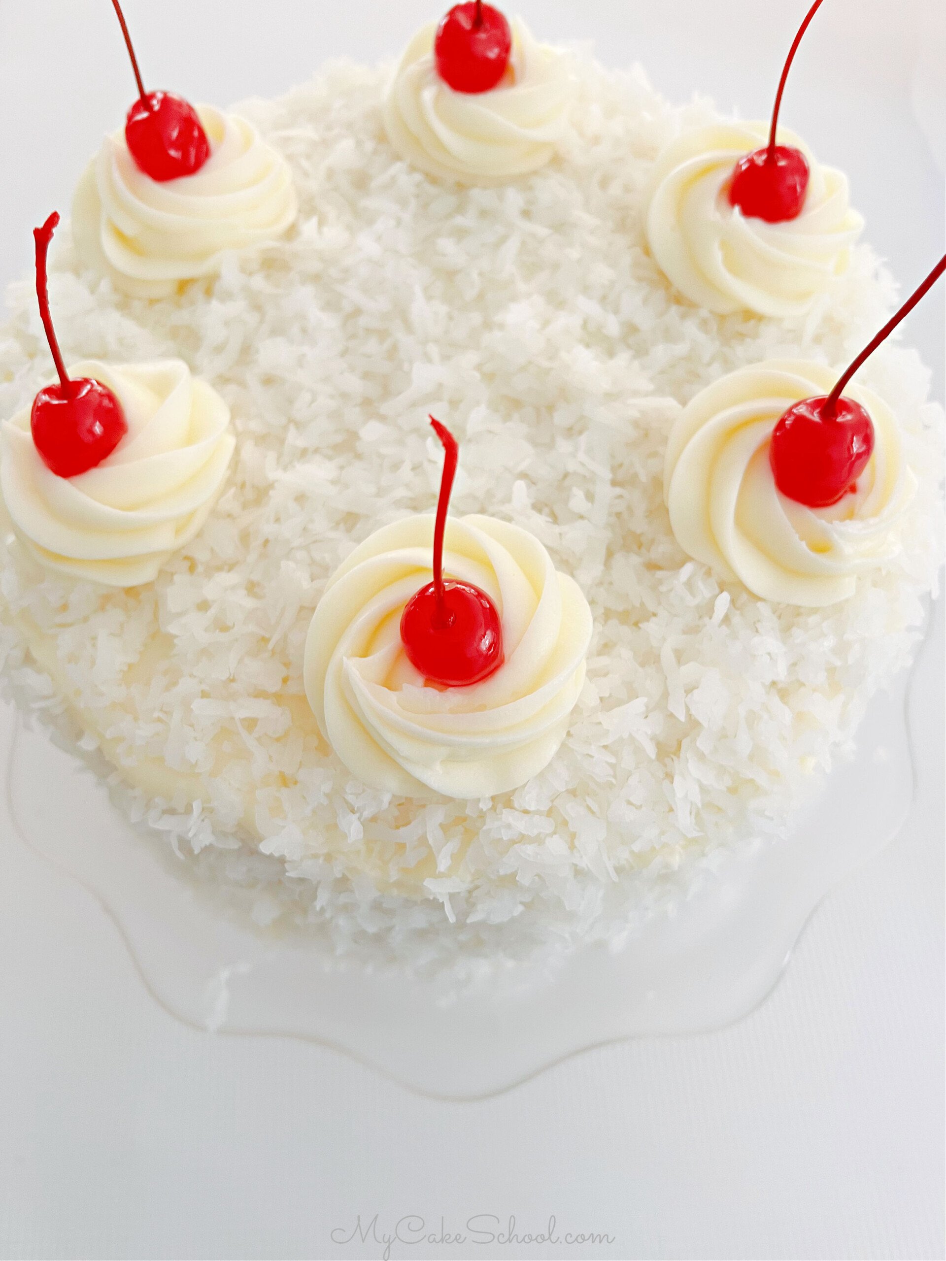 Top view of the Pina Colada Cake, with piped rosettes of cream cheese frosting around the edge, topped with maraschino cherries.