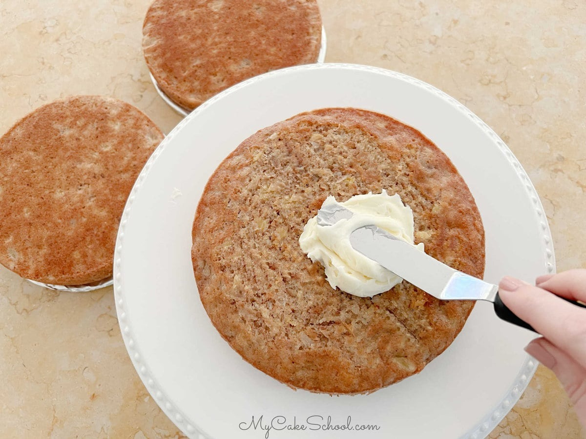 Spreading frosting on a hummingbird cake layer.