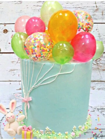 Gelatin Balloons Cake. Blue frosted cake with colorful gelatin balloons on top, and fondant bunny holding the buttercream "strings".