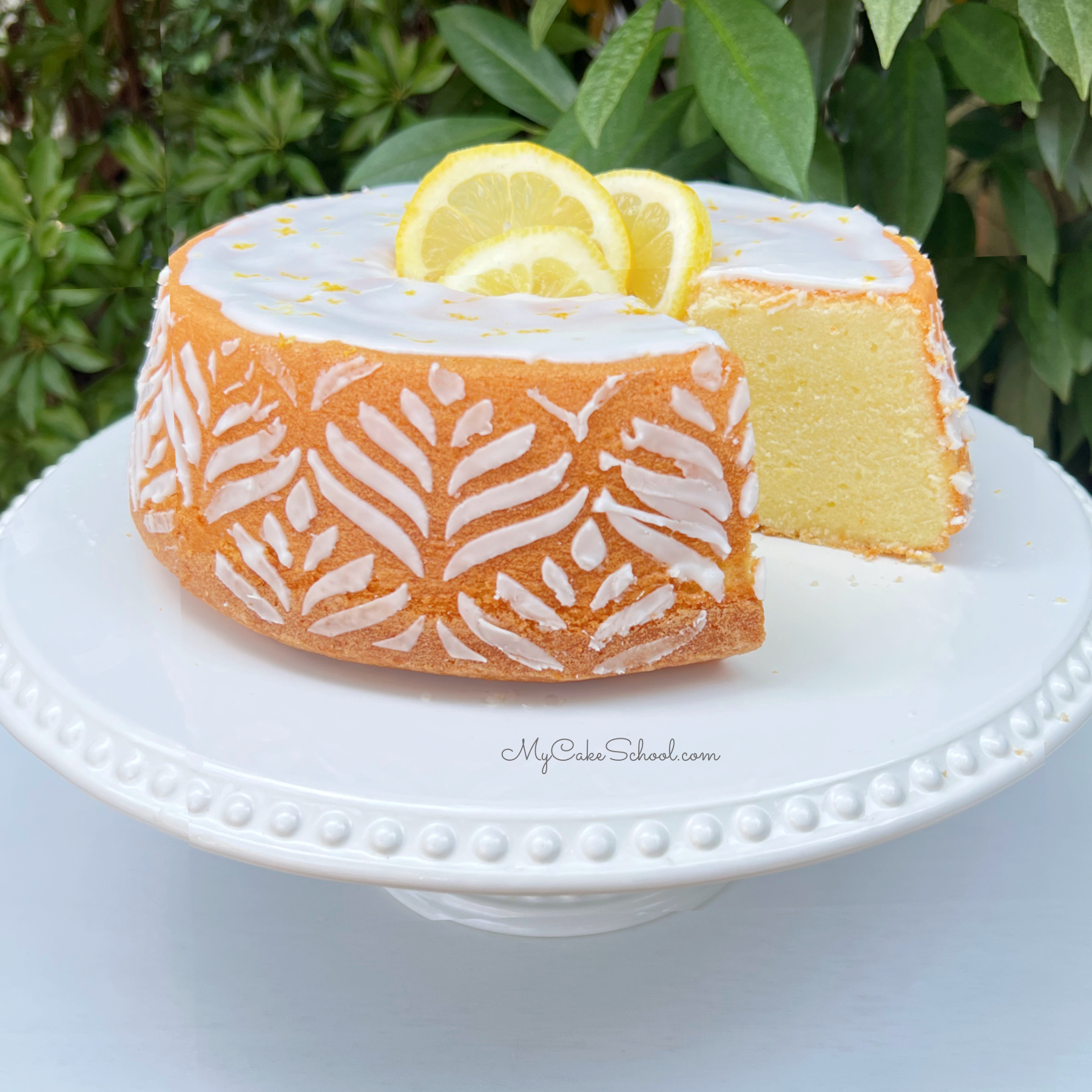 Lemon Pound Cake, with white sugar stenciling around the sides, and topped with lemon slices.