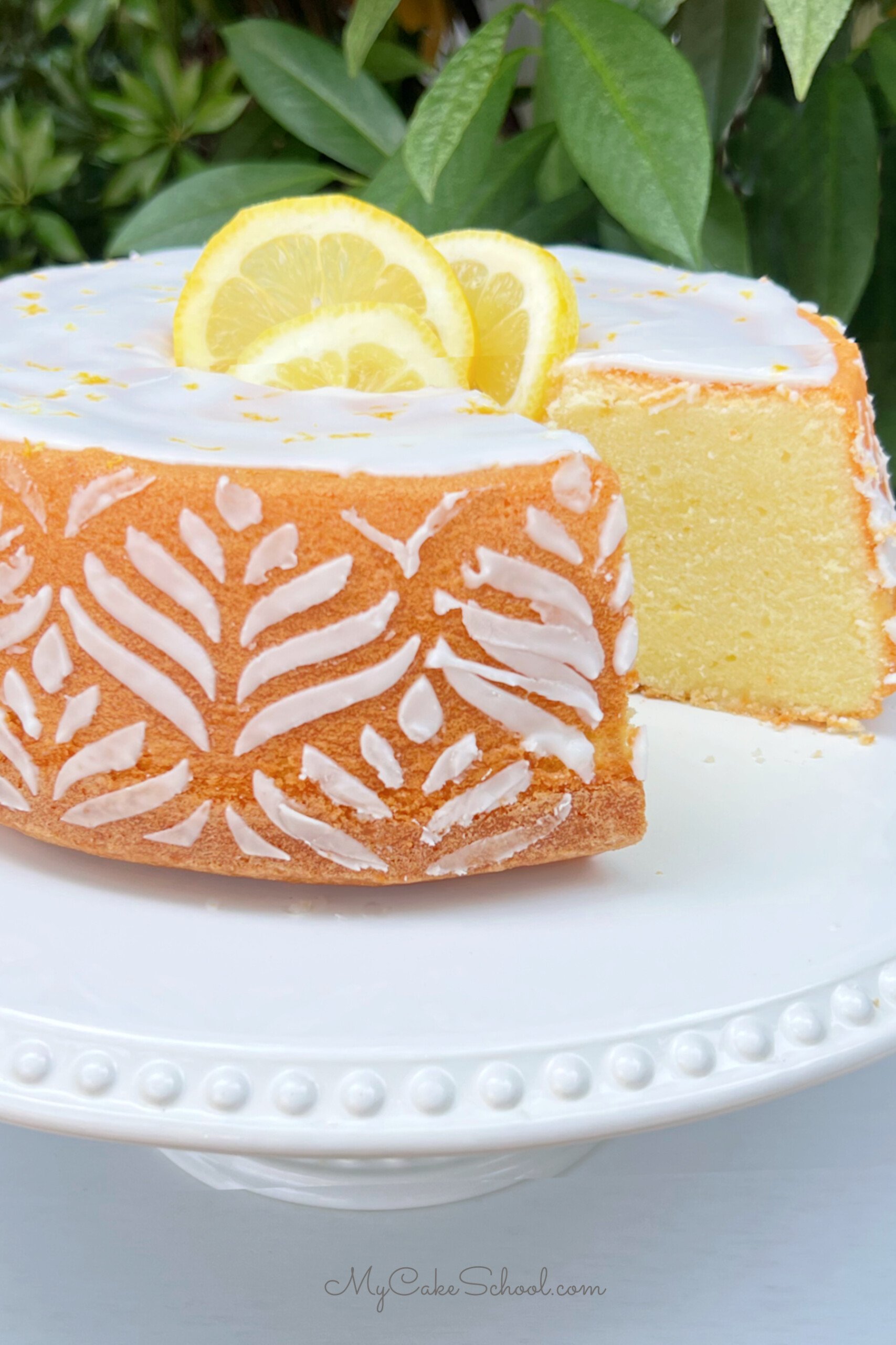 Sliced Lemon Pound Cake on a white pedestal with white stenciling around the sides.