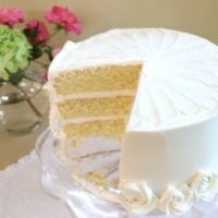 Vanilla Buttermilk Cake, sliced, on a glass pedestal.