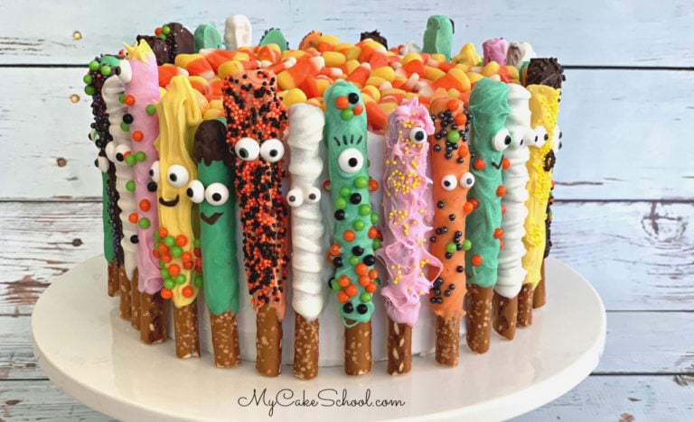 Colorful Pretzel Rods, decorated as monsters, wrapped around the sides of a cake.