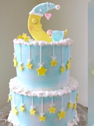 Moon and Stars themed Baby Shower Cake, on a cake pedestal. Light blue tiered cake with topper featuring baby sleeping on a crescent moon.