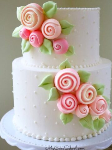 White frosted, two tiered cake with cascade of pink rose meringues applied diagonally to the front of the cake.