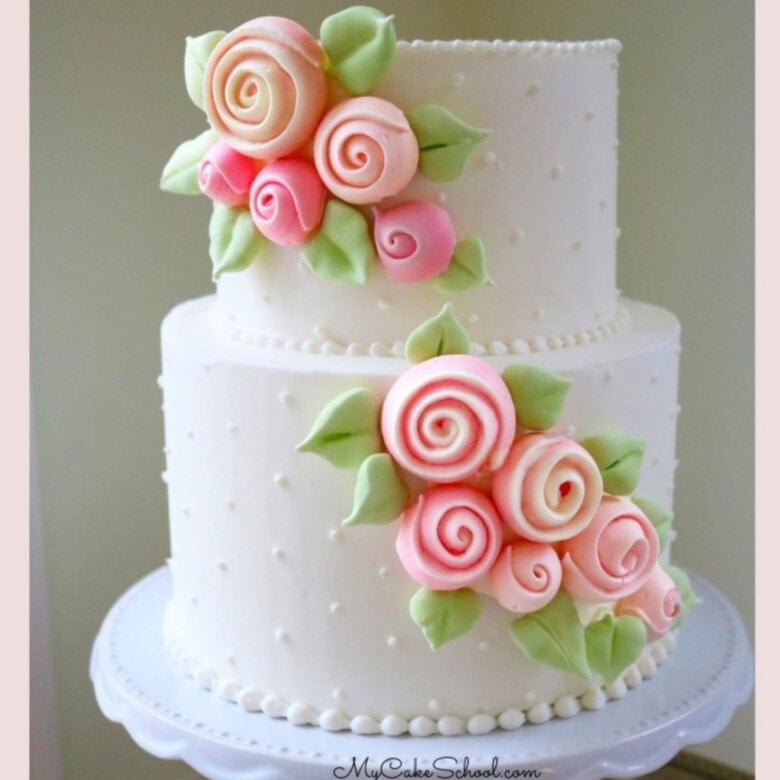 White frosted, two tiered cake with cascade of pink rose meringues applied diagonally to the front of the cake.