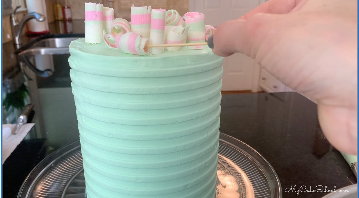 Adding chilled curls to top of cake with toothpick