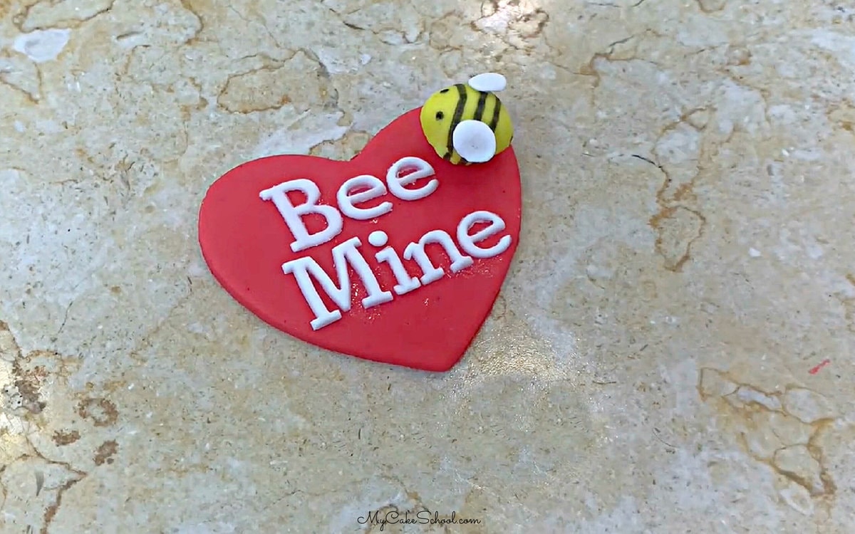 Bee Mine message on a red fondant heart with small yellow bee also attached