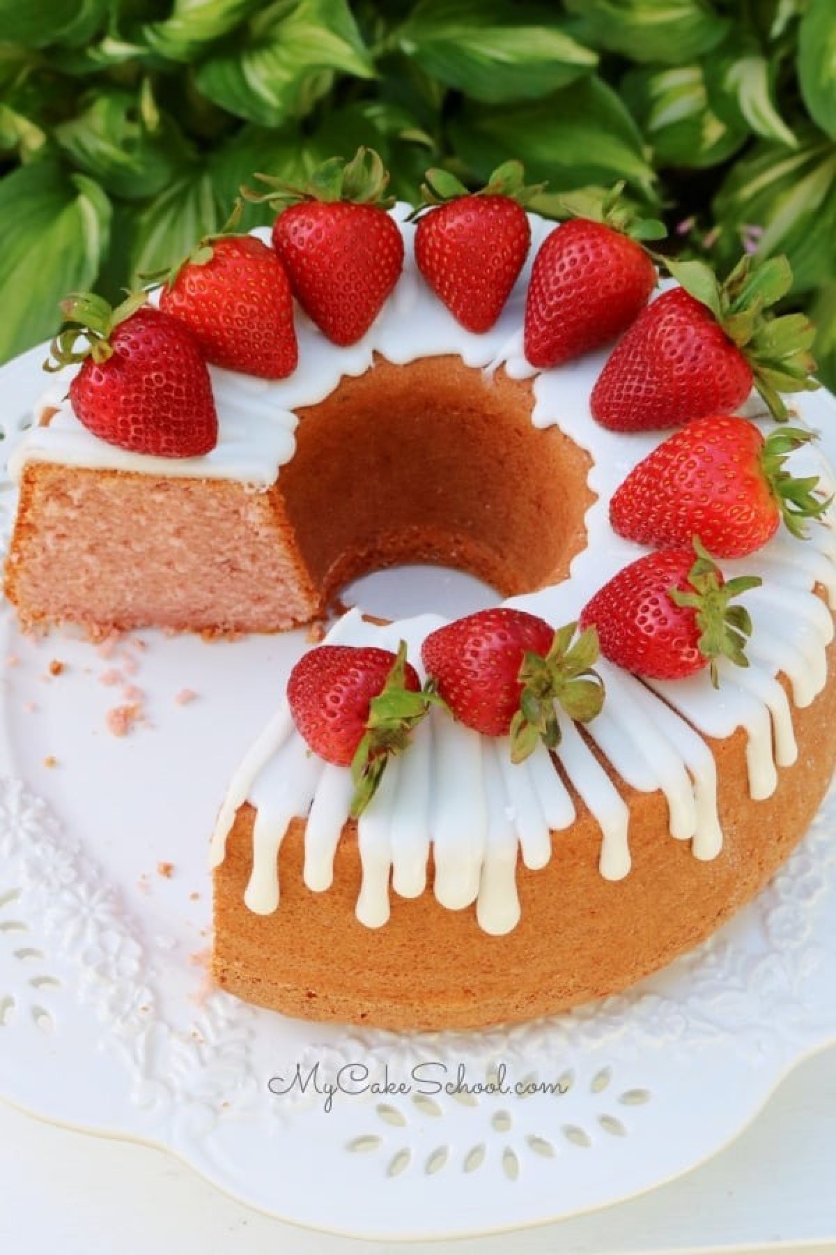 Sliced Strawberry Pound Cake, topped with fresh strawberries, on white pedestal.