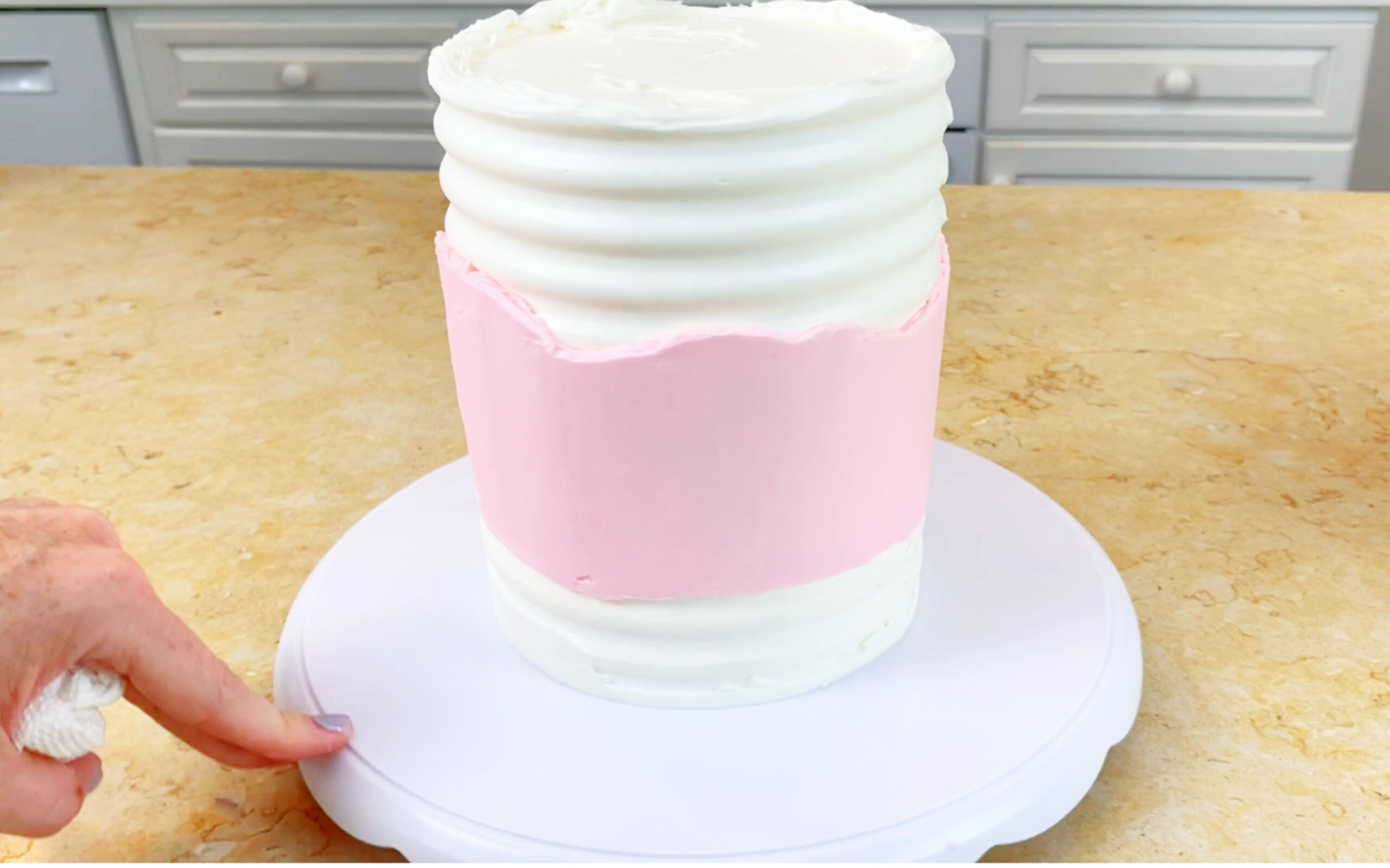 Combed white buttercream cake with smooth pink buttercream section around the middle.