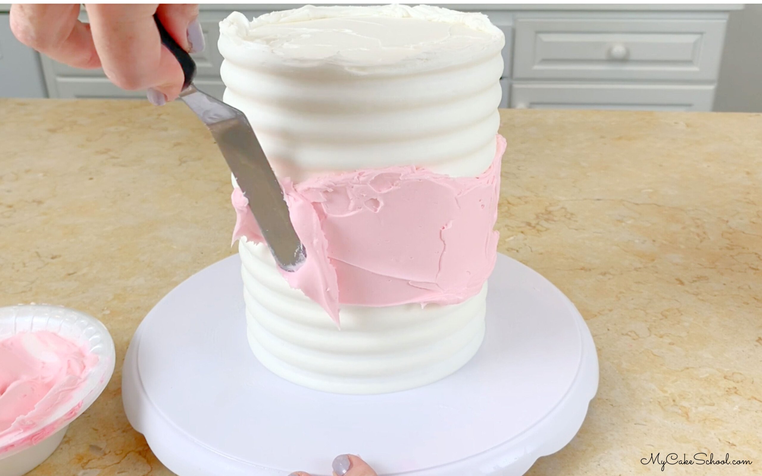 Adding light pink buttercream to the mid section of the cake around the sides.