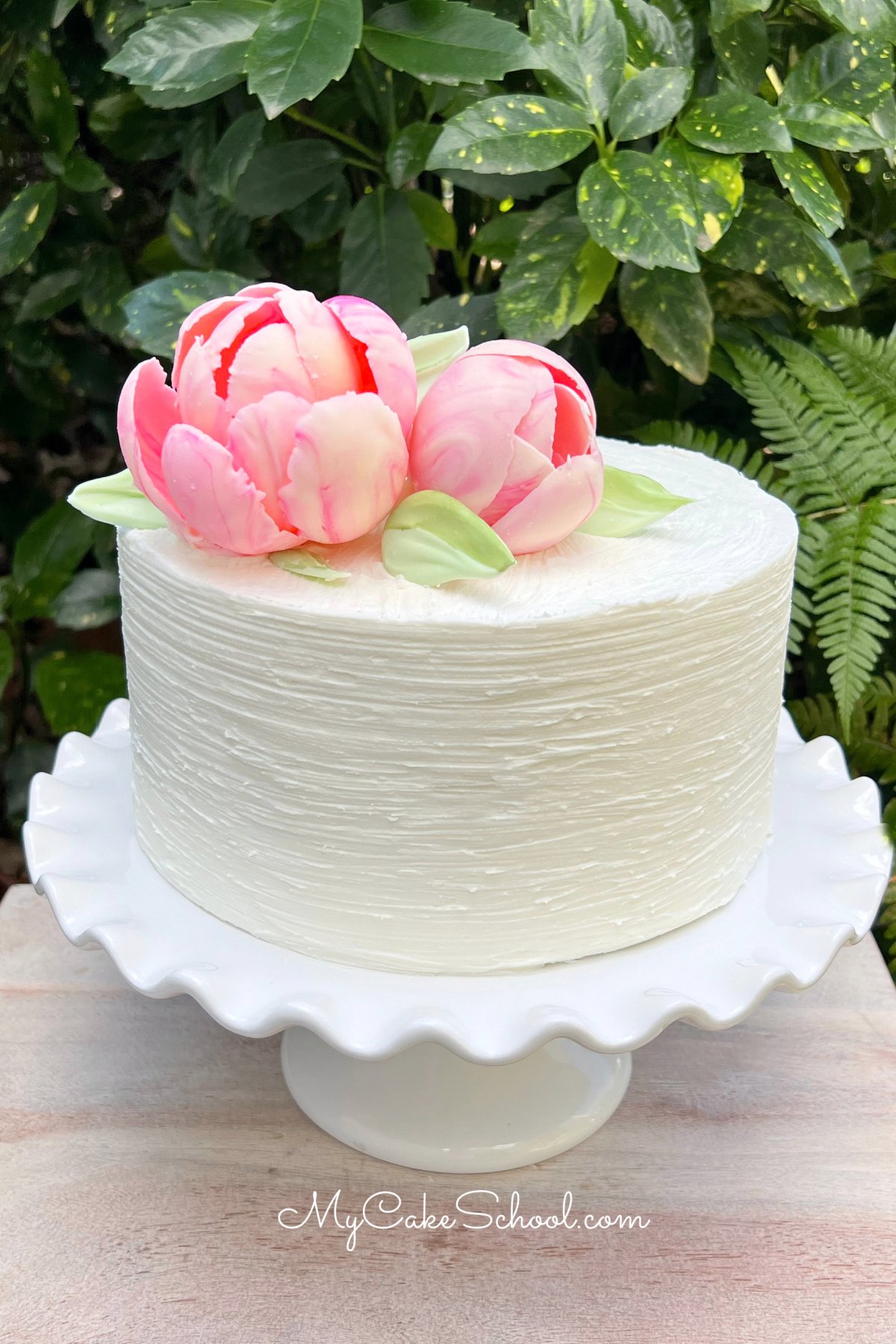 Cake frosted in vanilla buttercream, topped with two large pink chocolate flowers.