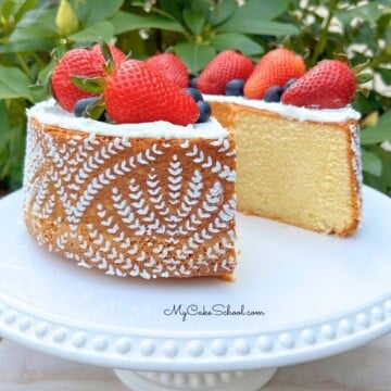 Sliced whipping cream pound cake on a pedestal, topped with fresh strawberries.