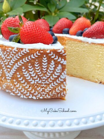 Sliced whipping cream pound cake on a pedestal, topped with fresh strawberries.