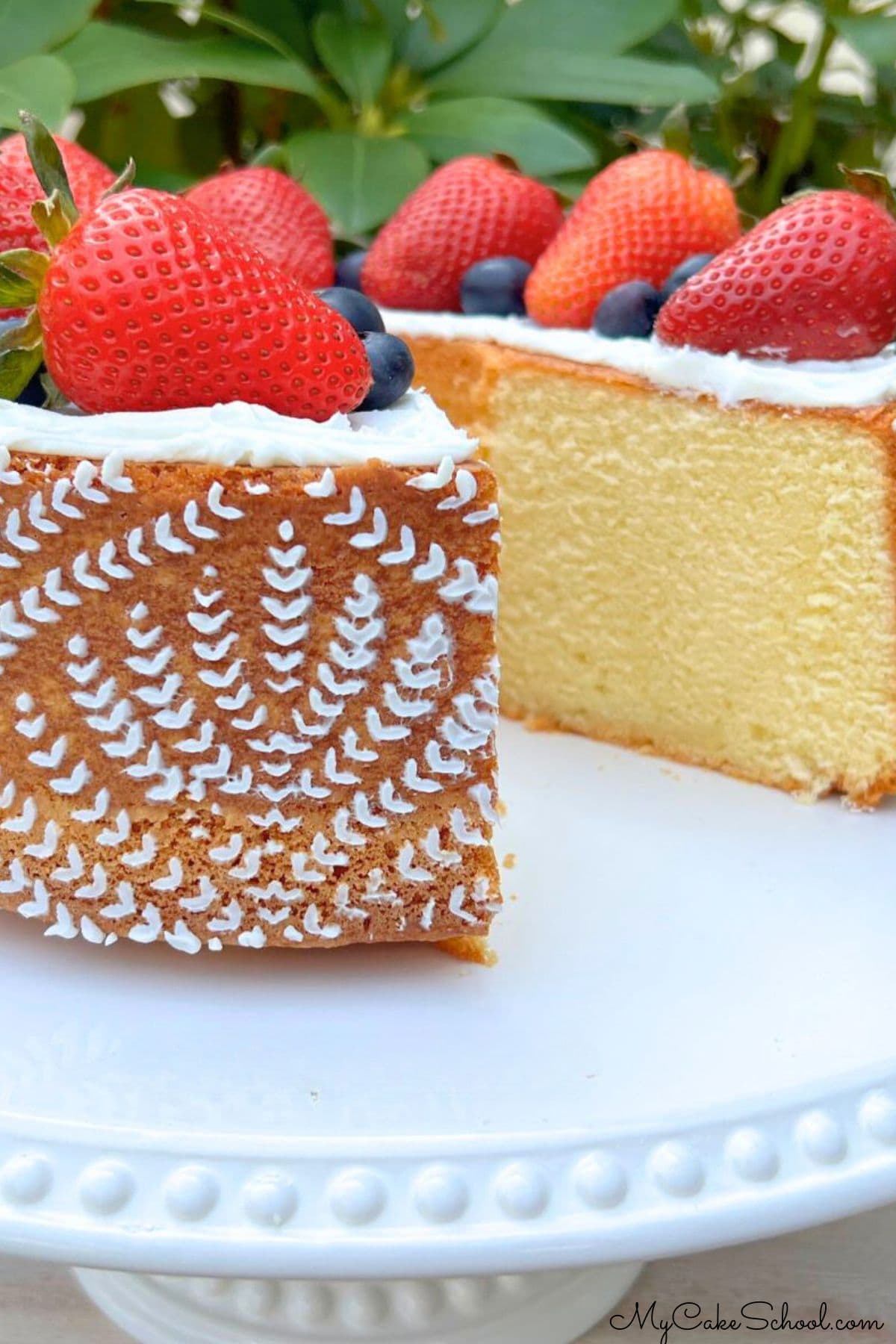 Sliced whipping cream pound cake on a pedestal, topped with fresh strawberries.