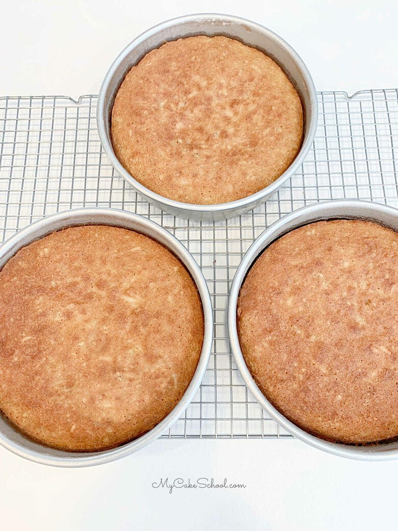 Cake layers cooling on a wire rack in the cake pans