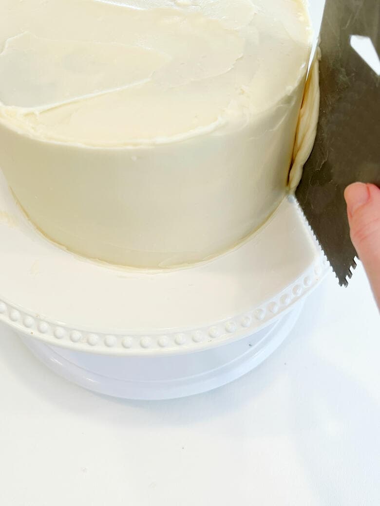 Smoothing the frosting around the sides of the cake with a metal bench scraper