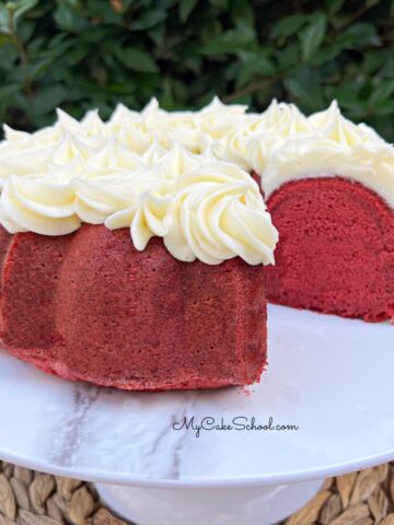 Red velvet pound cake on a white pedestal, topped with cream cheese piping.