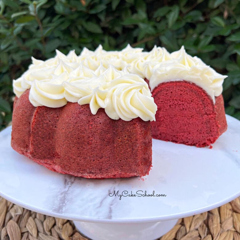 Red velvet pound cake on a white pedestal, topped with cream cheese piping.