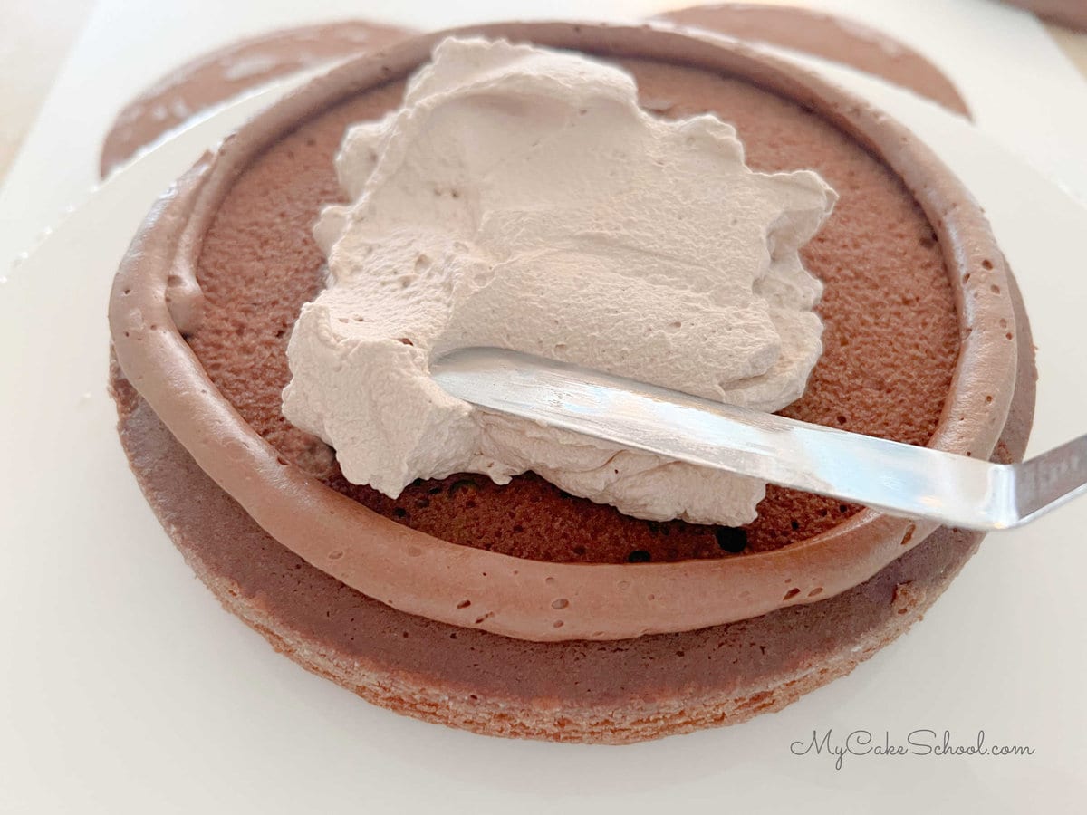 Spreading top of cake layer with chocolate whipped cream, within a buttercream dam