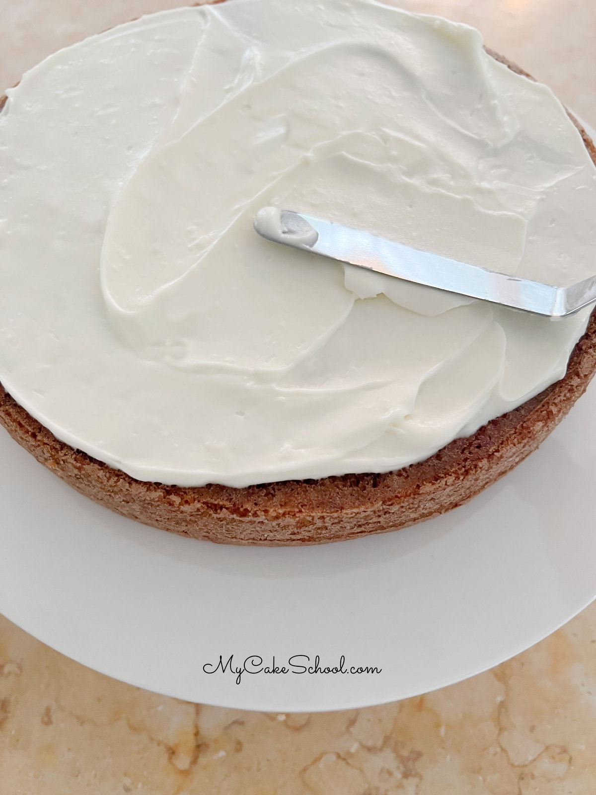 Frosting bottom carrot cake layer with a thin layer of cream cheese frosting.