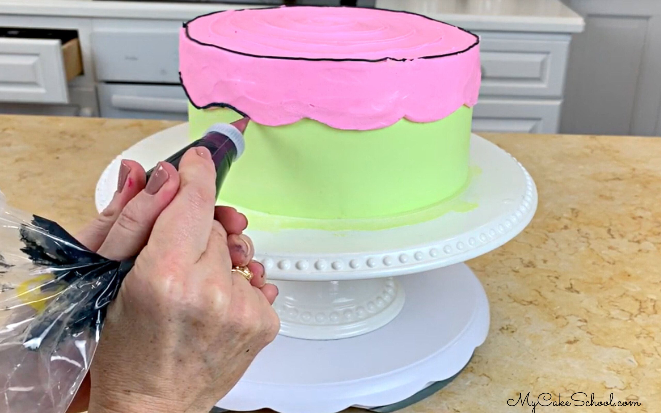 Adding black buttercream outlines to the cartoon cake with a small round piping tip.