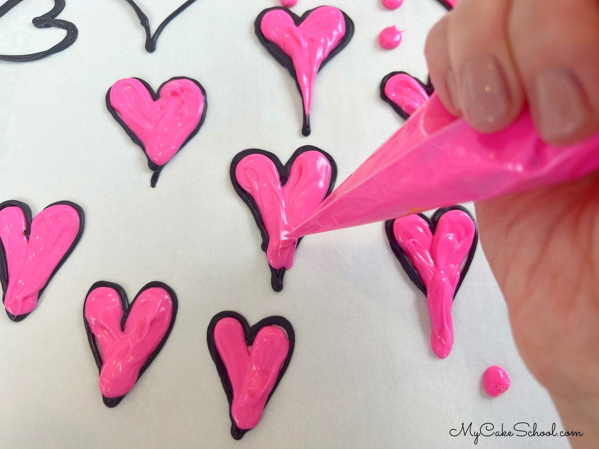 Piped candy coating hearts on a parchment lined cookie sheet