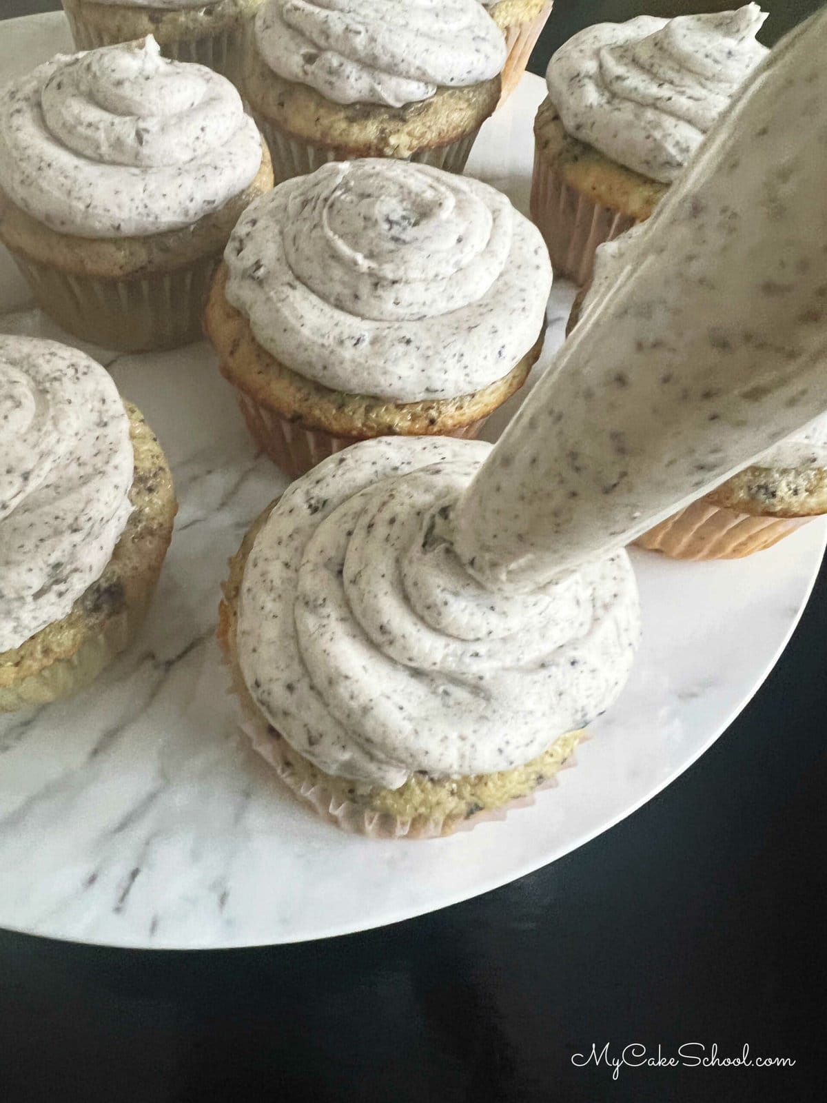 Piping swirls of Oreo Buttercream on top of Cupcakes