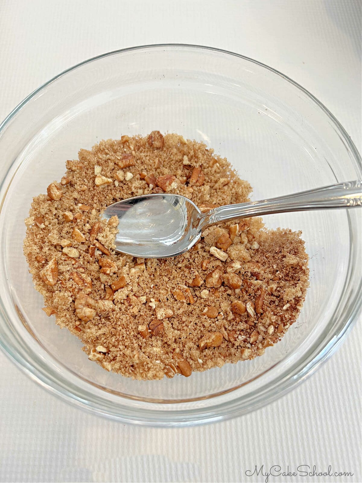 Glass bowl filled with cinnamon, brown sugar, and pecan mixture along with a spoon