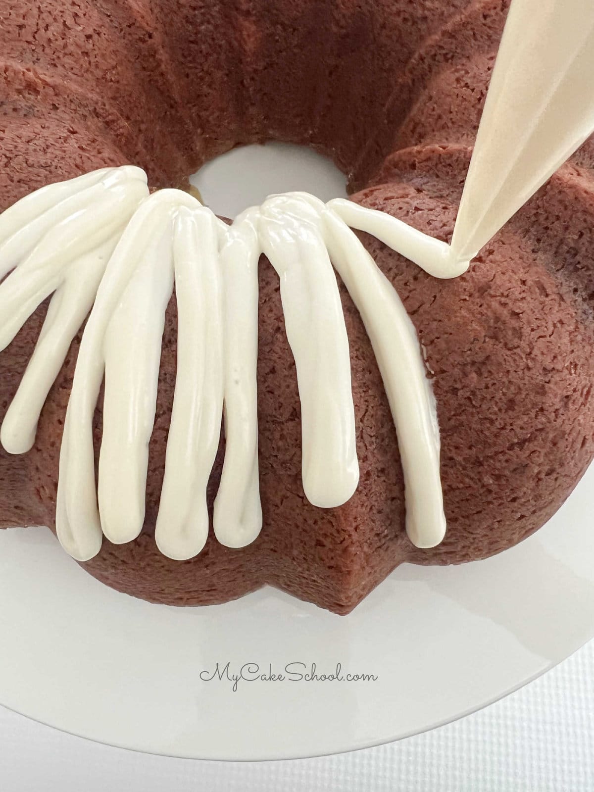 Piping cream cheese glaze onto the hummingbird bundt cake