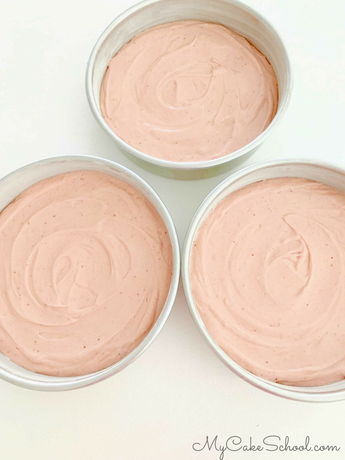 Three cake pans filled with pink cake batter