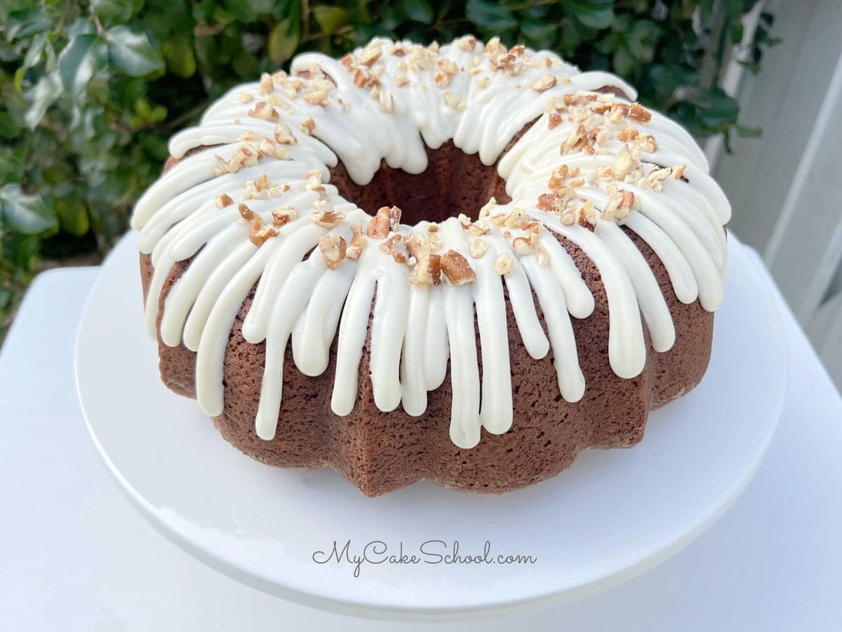 Hummingbird Cake with Cream Cheese Glaze, topped with pecans on a white pedestal