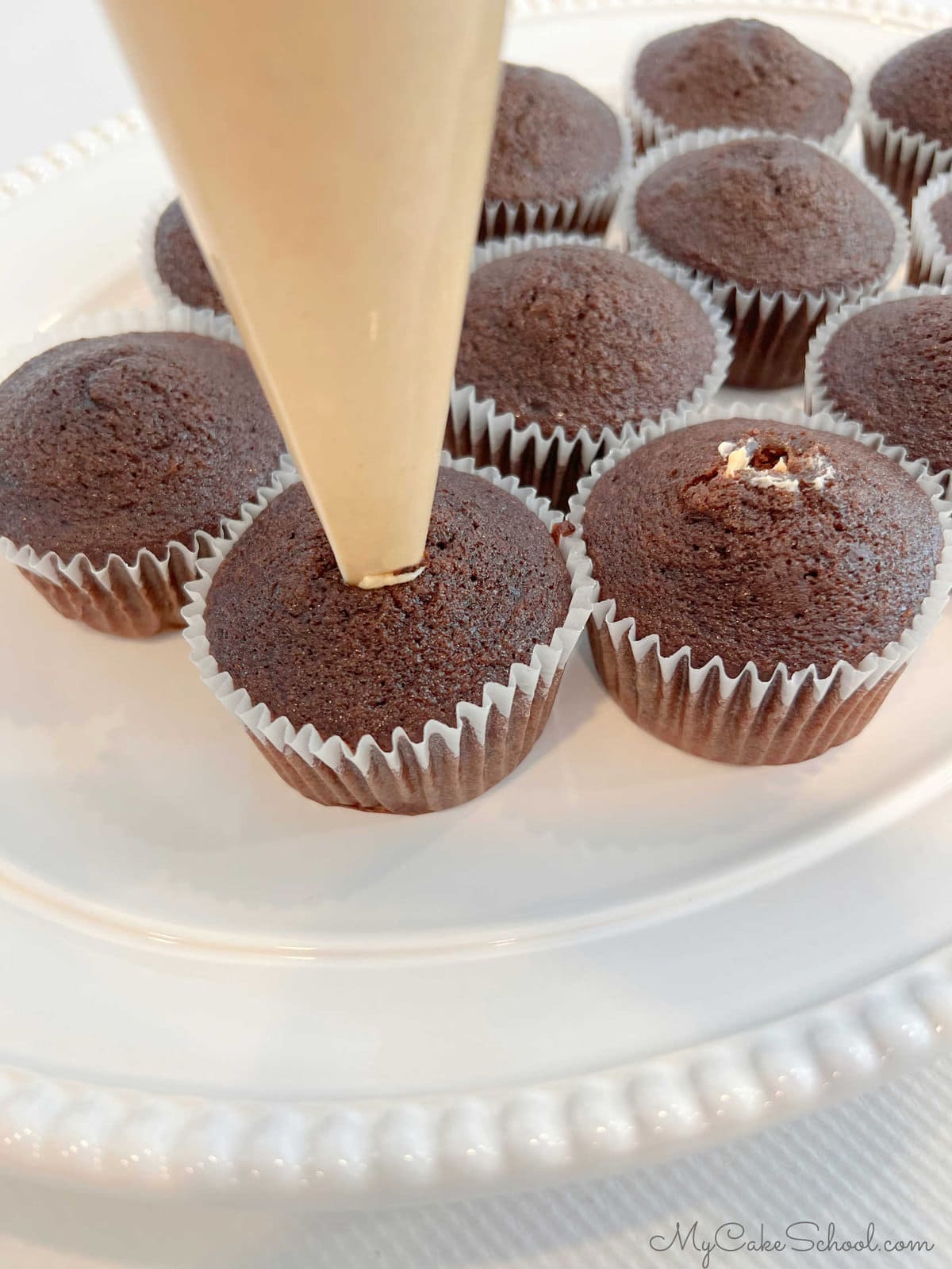 Filling chocolate cupcakes with piping bag of peanut butter frosting