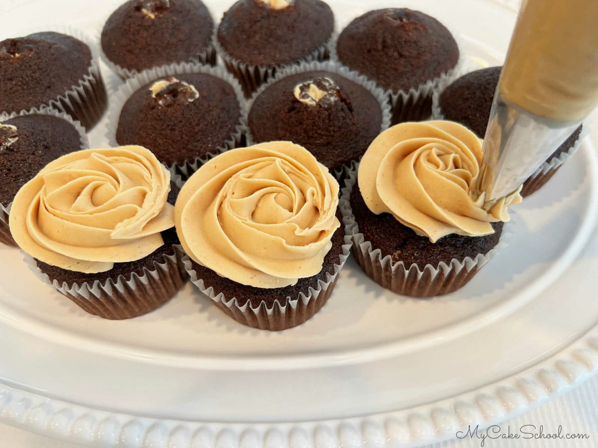 Piping swirls of frosting onto chocolate cupcakes