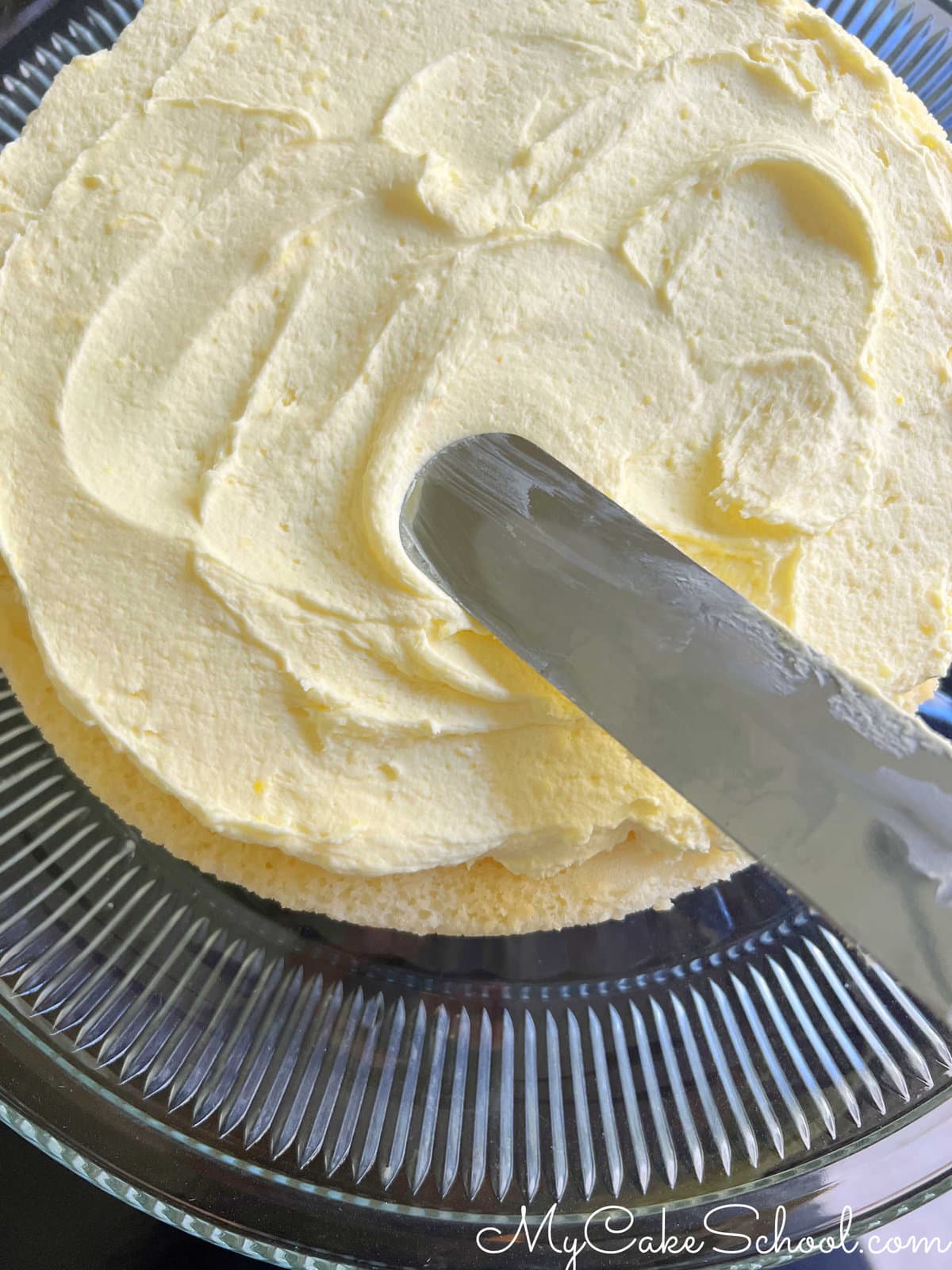Applying the lemon cream filling to the top of the first cake layer with a spatula, as the cake is being assembled