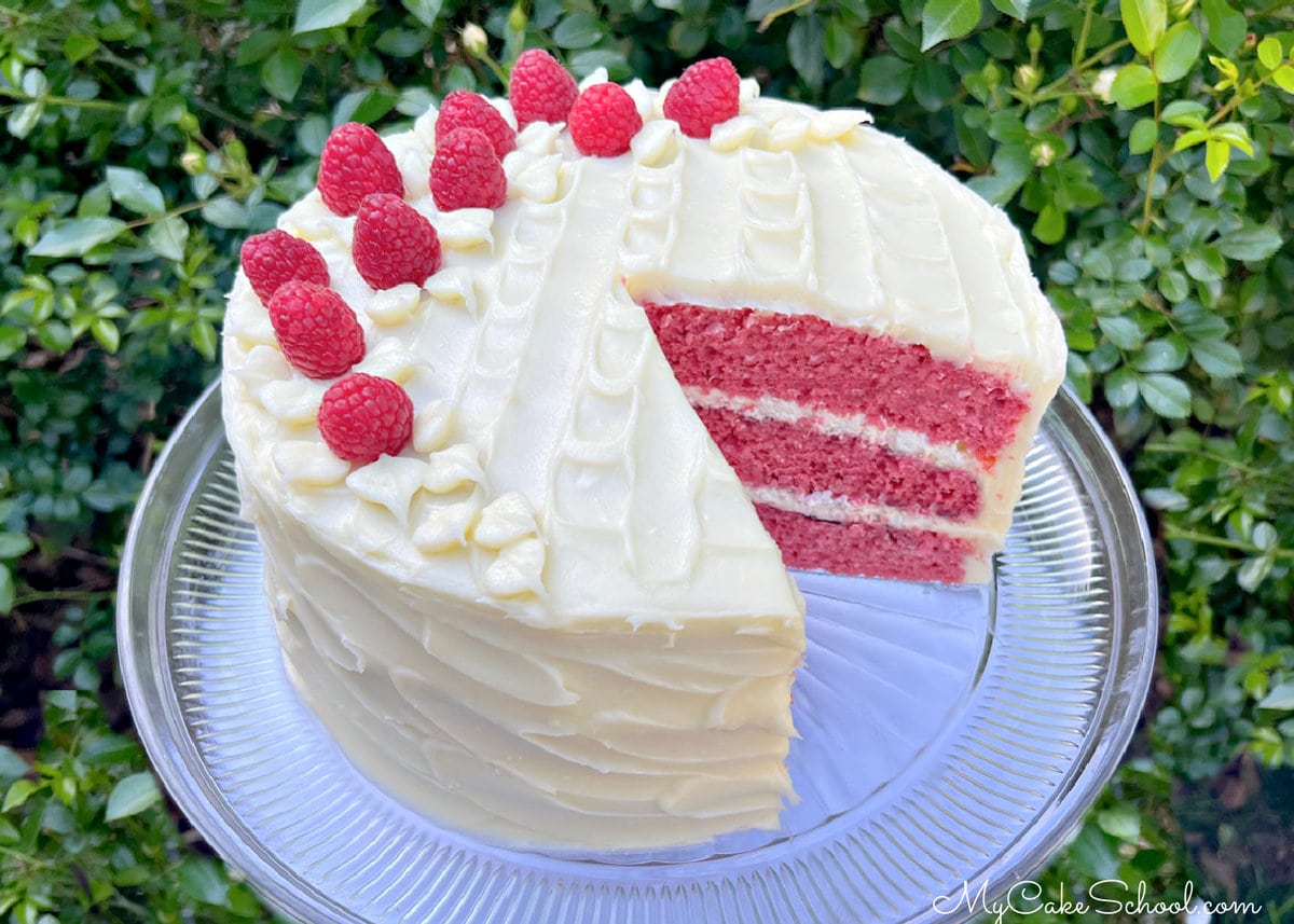 Sliced raspberry cake on a pedestal, topped with fresh raspberries