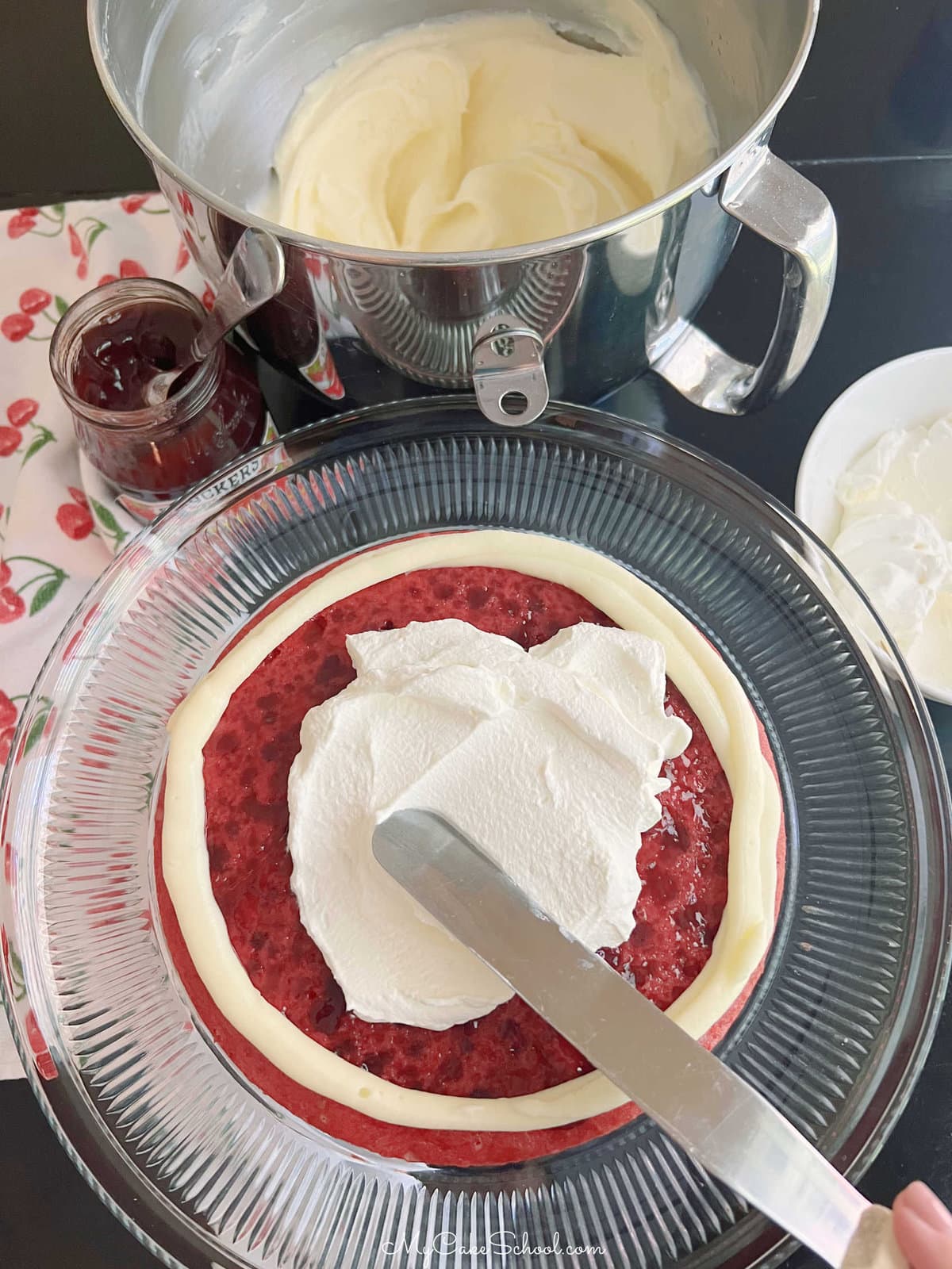 Spreading whipped cream filling over raspberry cake layer glazed with jam.