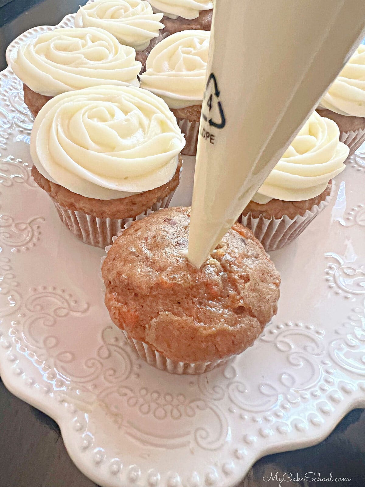 Inserting frosting-filled piping bag halfway into unfrosted cupcake