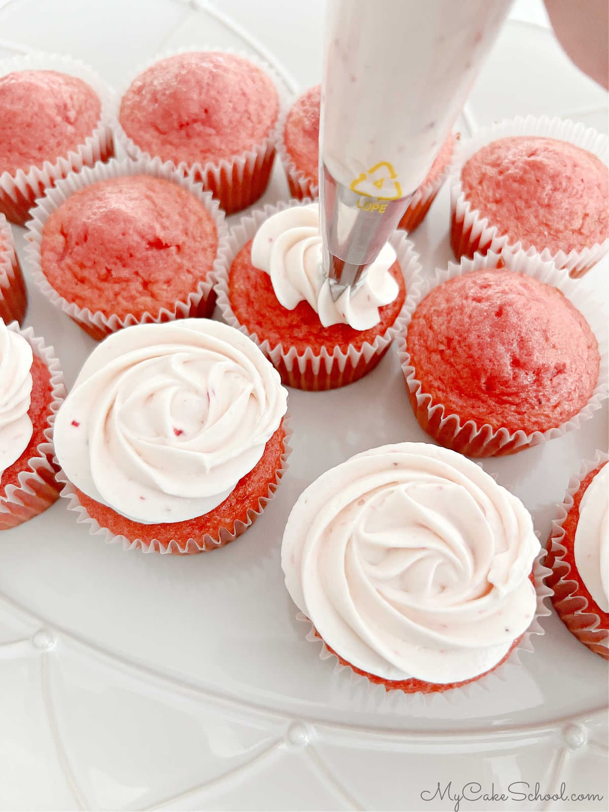 Piping frosting onto strawberry cupcakes using a 1M star tip