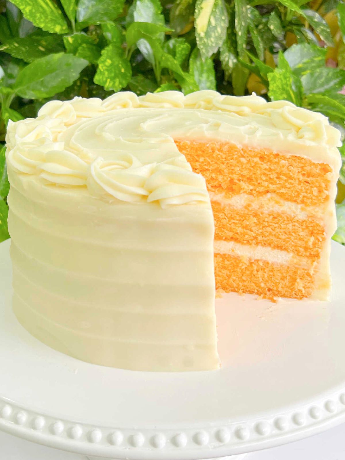 Sliced orange cake, filled and frosted with cream cheese frosting, on a white pedestal.