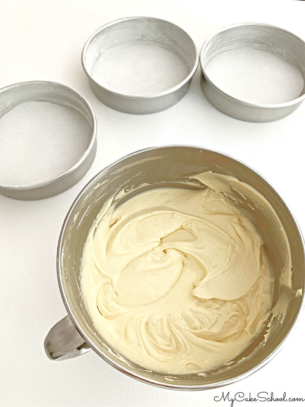 Bowl of Buttermilk Pound Cake batter along with three prepared 8 inch round cake pans