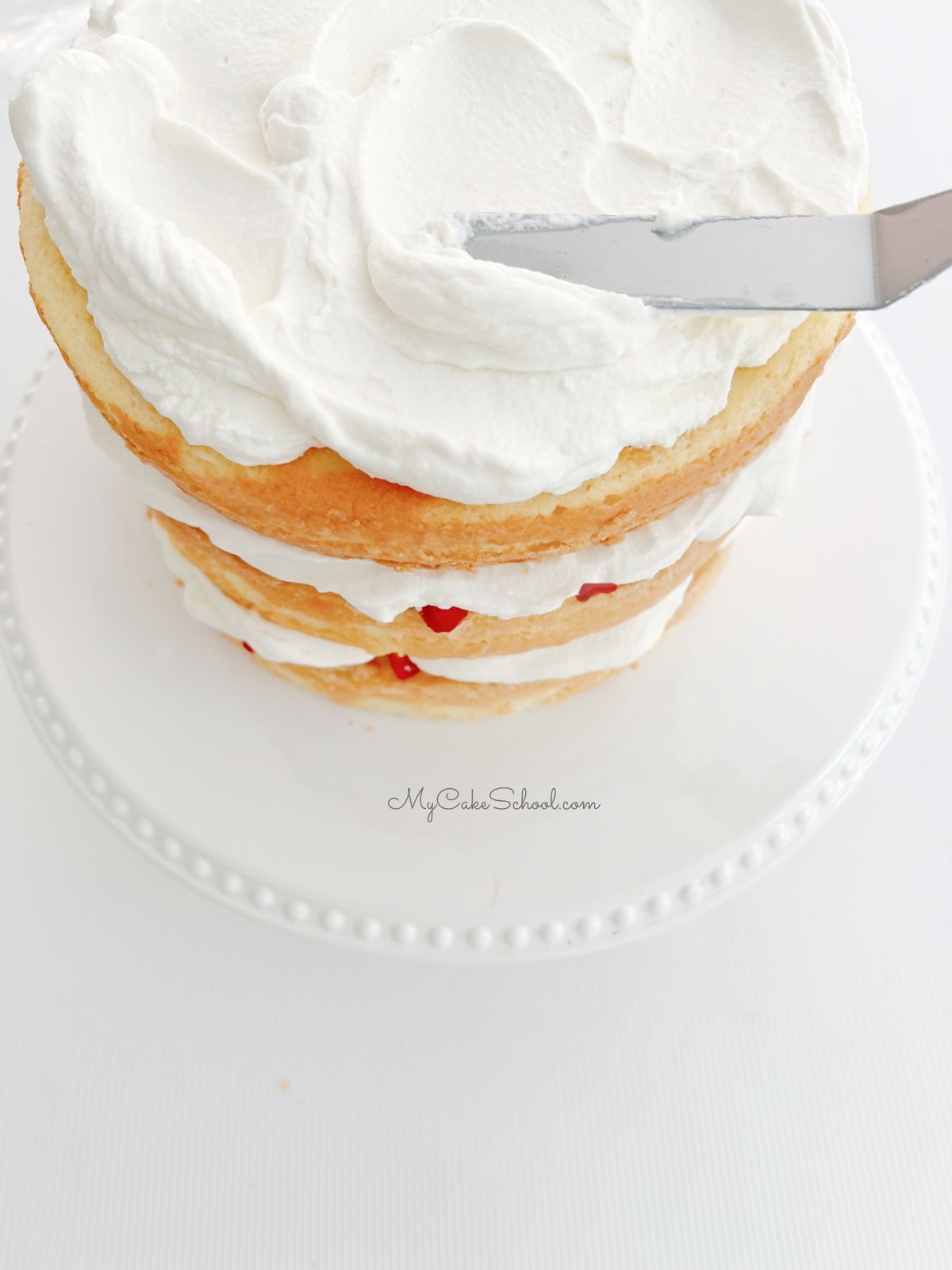 Topping the layered strawberry shortcake cake with whipped cream