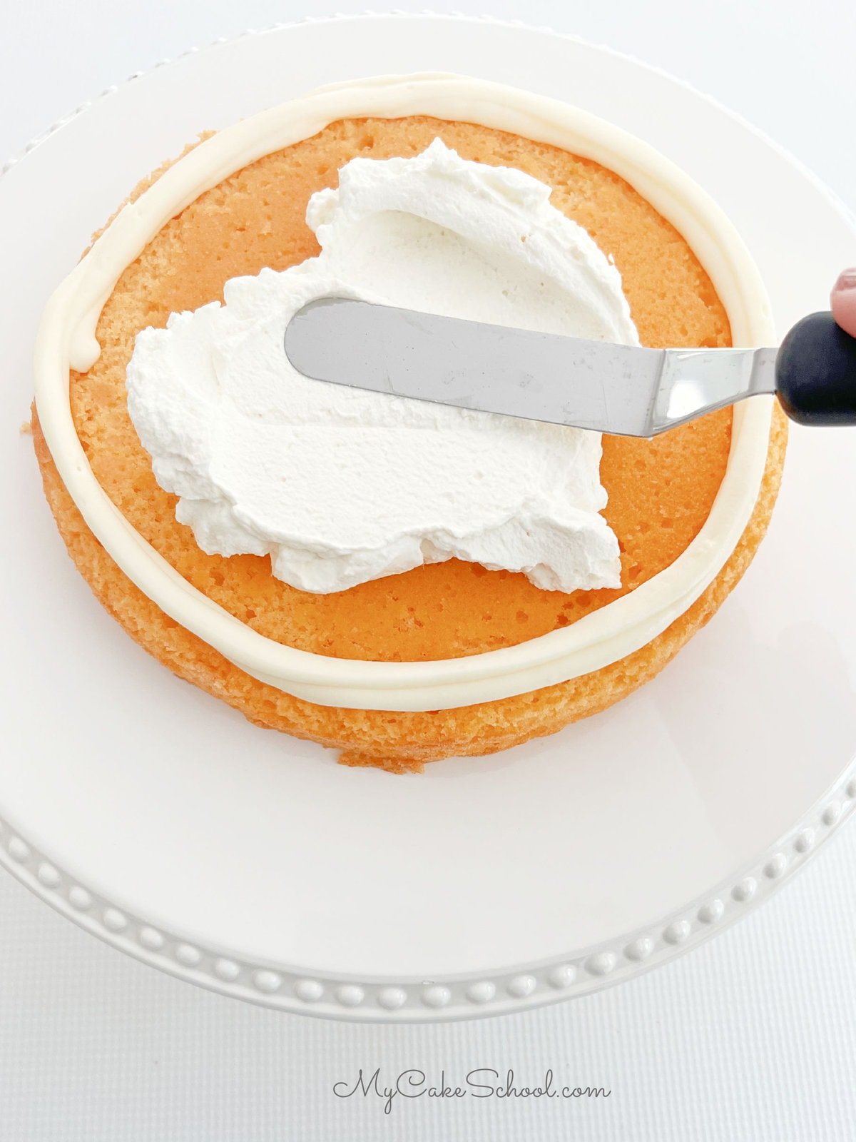 Spreading whipped cream within the frosting dam on the orange cake layer.